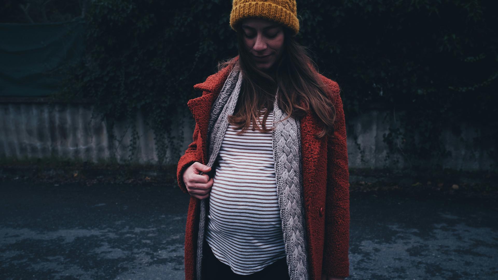 Eine schwangere Frau steht in einer düsteren Umgebung.