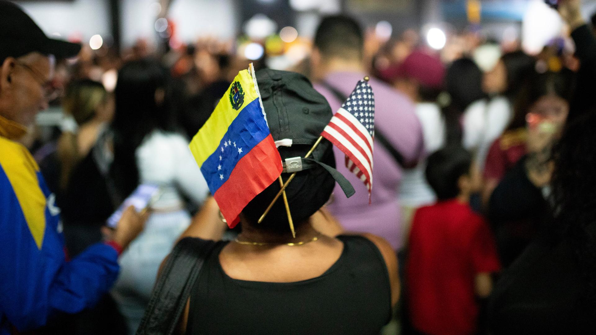 Fähnchen von Venezuela und den USA stecken in einer Kappe einer Frau inmitten einer Menschenmenge