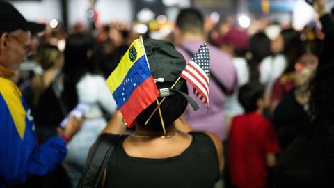 Fähnchen von Venezuela und den USA stecken in einer Kappe einer Frau inmitten einer Menschenmenge