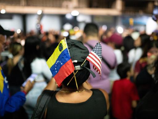 Fähnchen von Venezuela und den USA stecken in einer Kappe einer Frau inmitten einer Menschenmenge