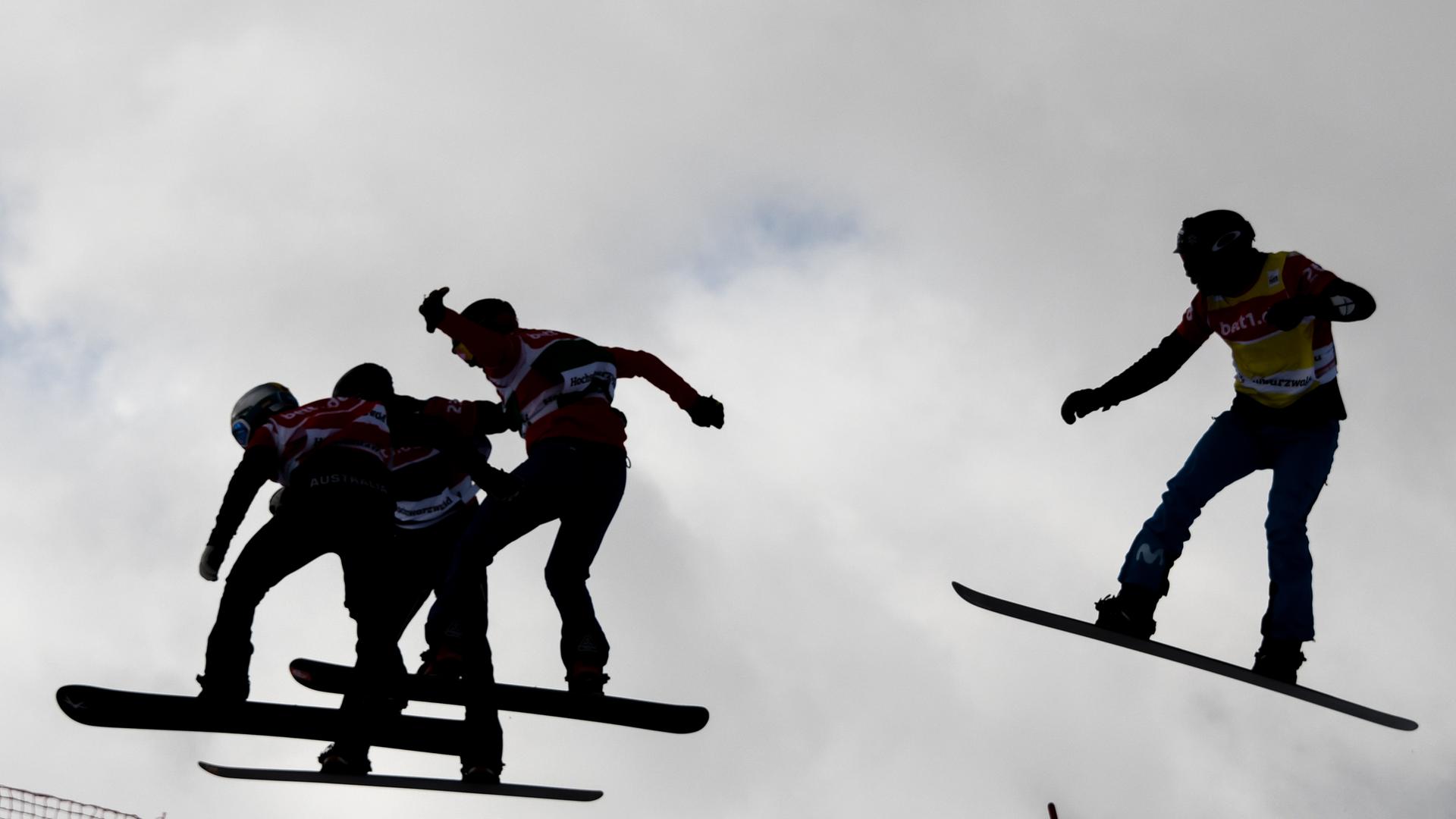 Snowboarder springen im Gegenlicht durch die Luft.