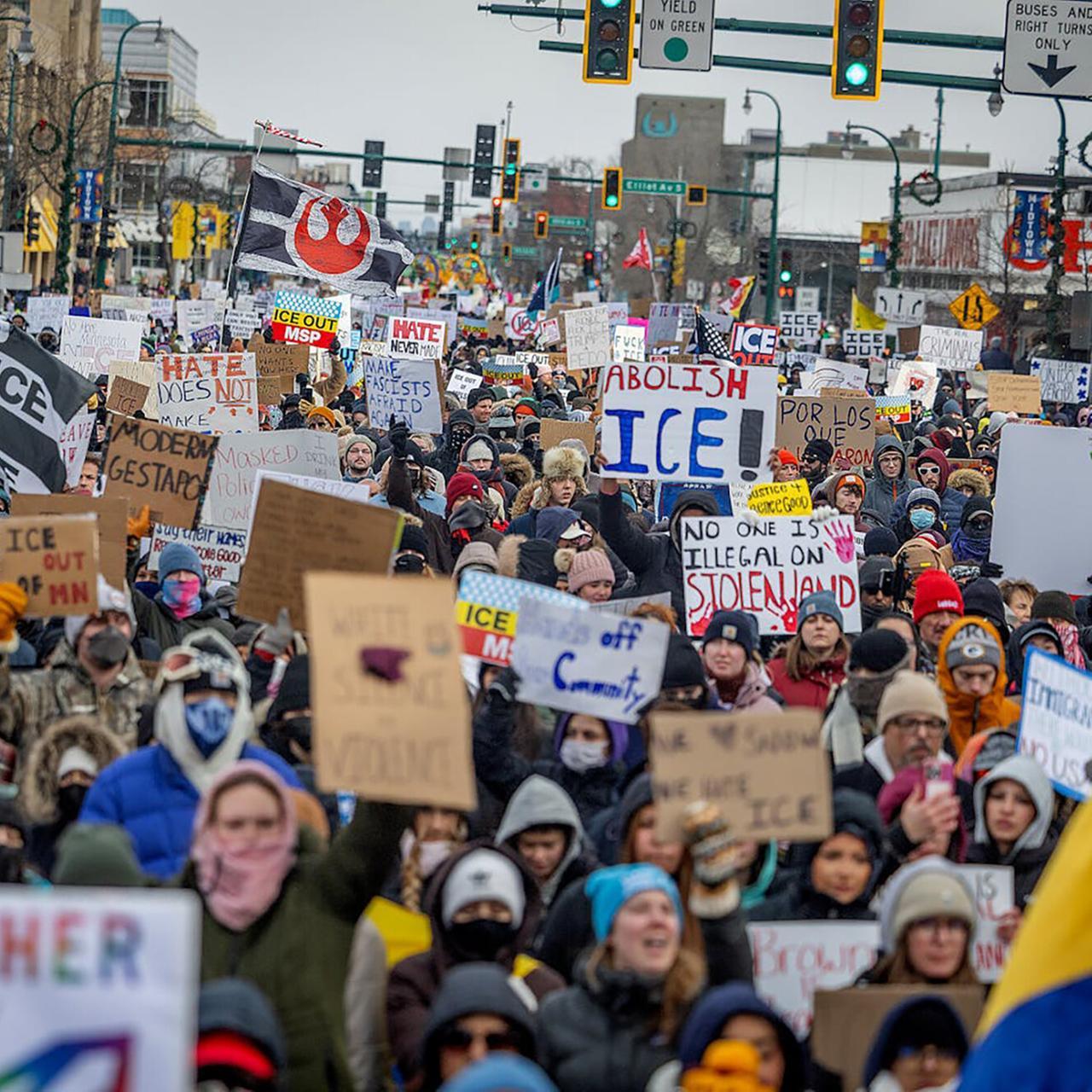 Blick von vorn auf eine riesige Menschenmenge mit Transparenten und Plaketen, die eine Straße entlangläuft.