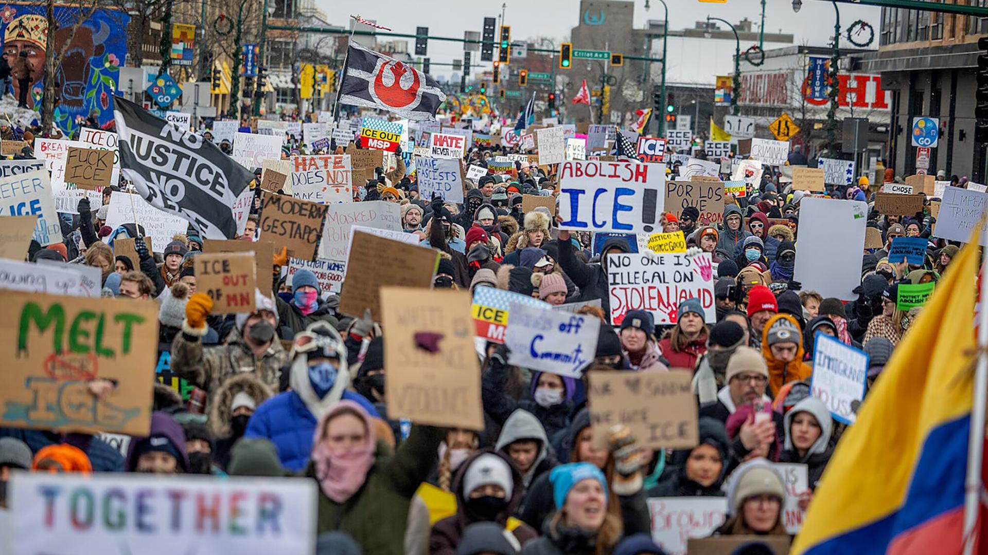Blick von vorn auf eine riesige Menschenmenge mit Transparenten und Plaketen, die eine Straße entlangläuft.