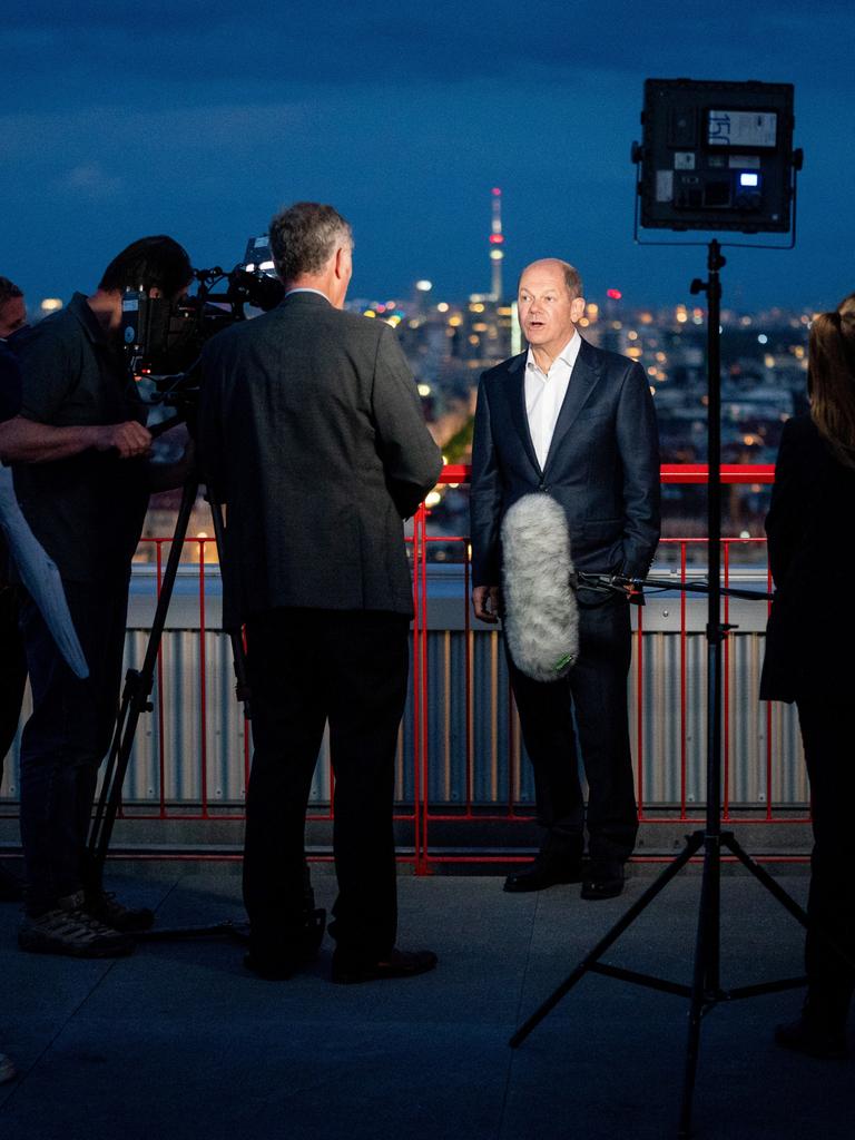 Olaf Scholz (SPD) steht 2021 vor der abendlichen Berliner Skyline auf einer Dachterasse und gibt dem Dokumentarfilmer Stephan Lamby (3.vl) ein Interview.