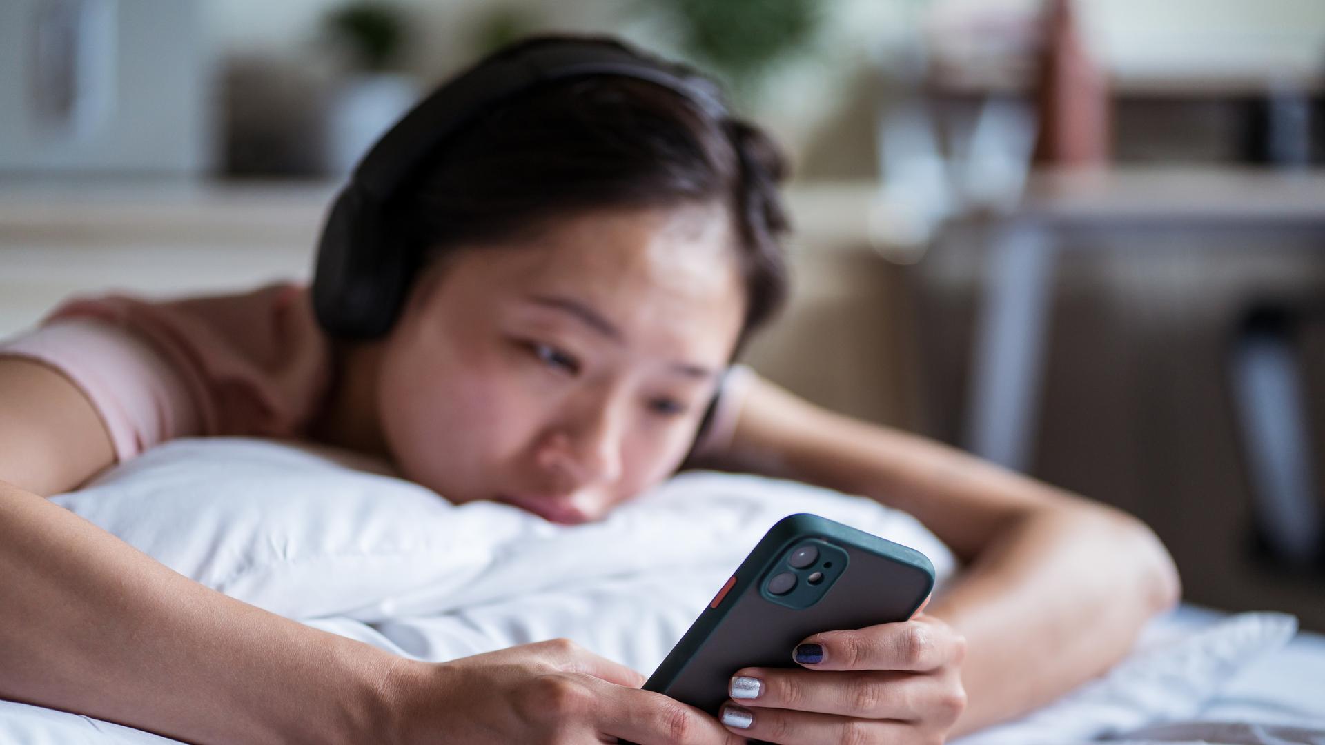 Traurige asiatische Frau, die auf dem Bett auf ihrem Smartphone surft