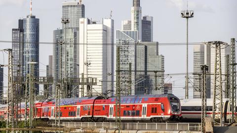 Hauptbahnhof mit Eisenbahnbrücke und Regionalzug vor der Skyline des Finanzzentrums von Frankfurt am Main.