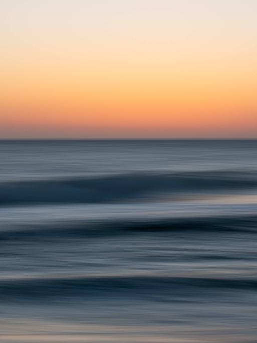 Abstrakte Langzeitbelichtung eines Sonnenuntergangs über dunkelblauen Meereswellen