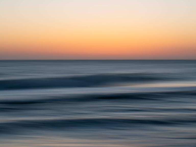 Abstrakte Langzeitbelichtung eines Sonnenuntergangs über dunkelblauen Meereswellen