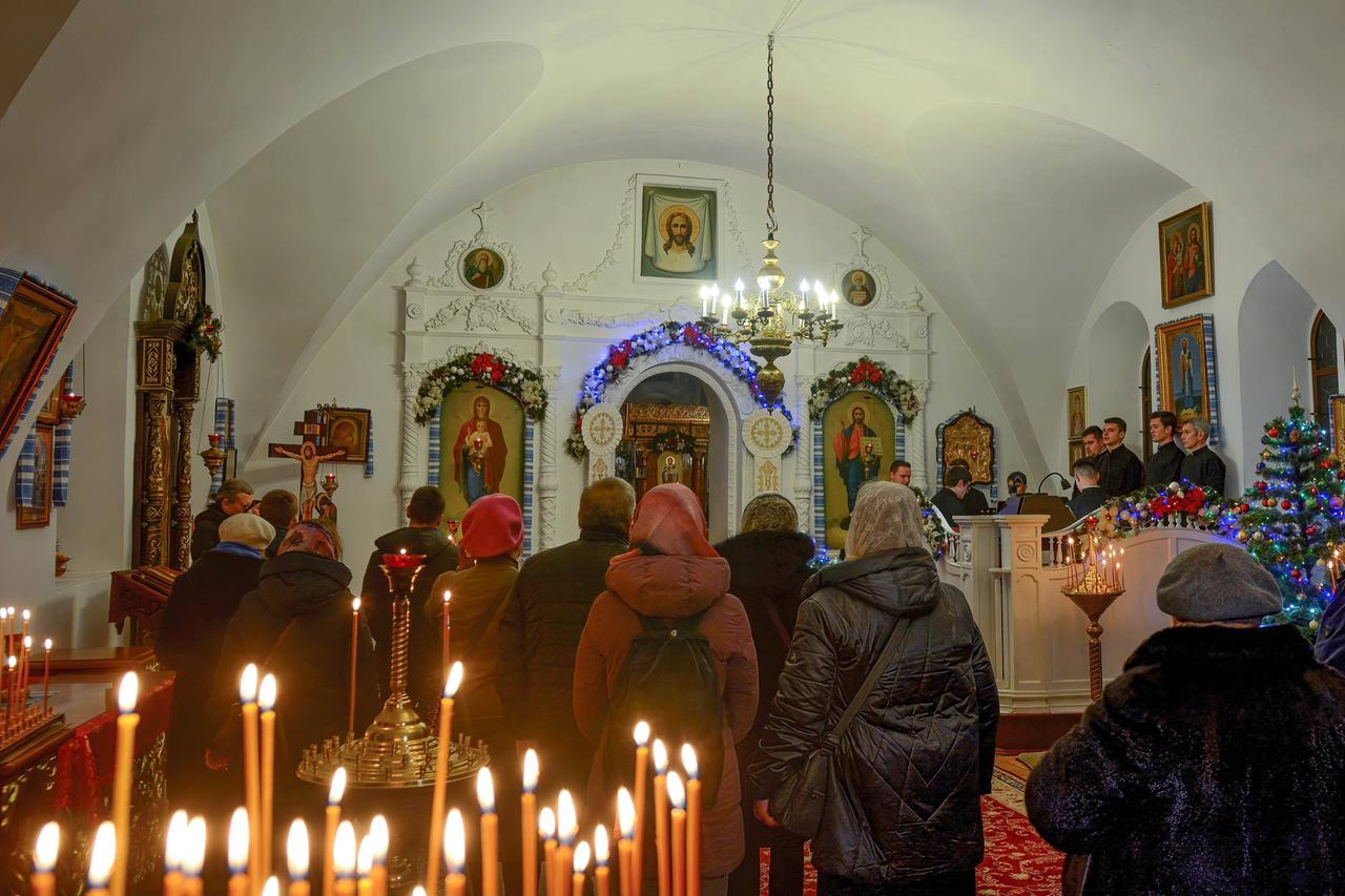 Die Menschen stehen in einer kleinen Kapelle. Im Vordergrund brennende Kerzen.