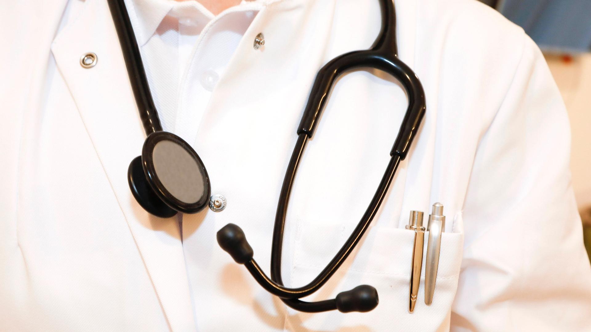 Um den Hals eines Arztes mit weißem Kittel hängt ein Stethoskop. 