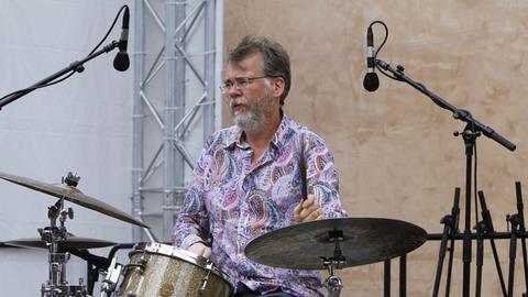 Oliver Strauch sitzt auf einer Bühne zwischen Mikrofonen an seinem Schlagzeug und spielt.