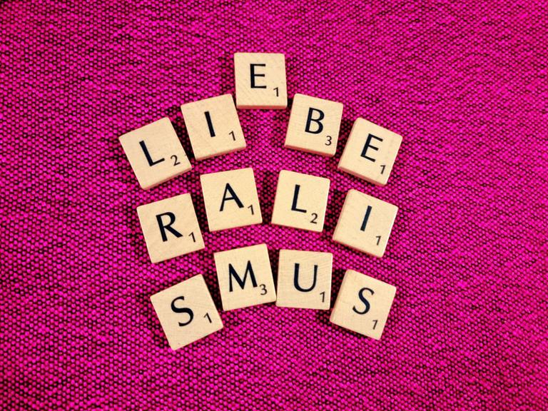 Scrabble-Buchstaben auf pinkem Untergrund bilden das Wort Liberalismus - zwischen dem I und dem B scheint sich ein E dazwischendrängeln zu wollen, das Wort Liebe wird angedeutet.