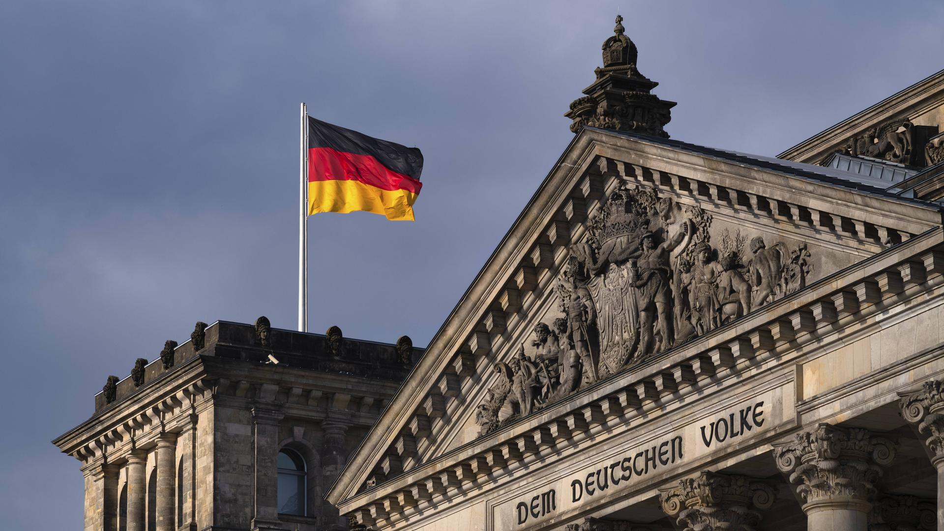 Die Flagge der BRD weht auf dem Reichstagsgebäude mit dem Schriftzug "DEM DEUTSCHEN VOLKE" und dem Relief im Tympanon über dem Hauptportal im Berliner Regierungsviertel Die Flagge der BRD weht auf dem Reichstagsgebäude mit dem Schriftzug "DEM DEUTSCHEN VOLKE" und dem Relief im Tympanon über dem Hauptportal im Berliner Regierungsviertel
