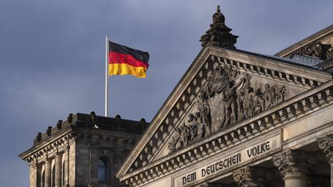 Die Flagge der BRD weht auf dem Reichstagsgebäude mit dem Schriftzug "DEM DEUTSCHEN VOLKE" und dem Relief im Tympanon über dem Hauptportal im Berliner Regierungsviertel