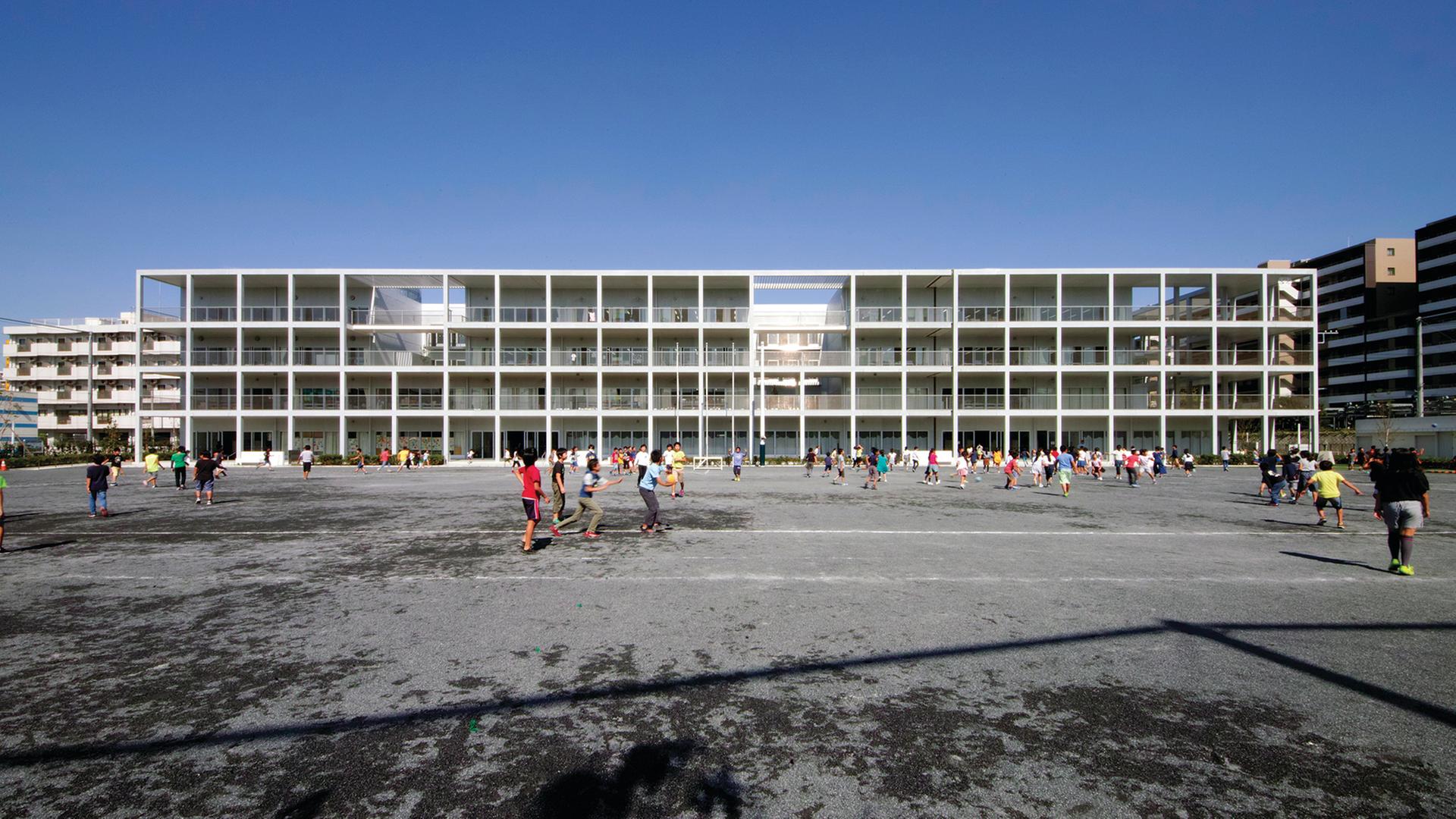 Ein fast gläsernes Gebäude, eine Schule, von dem japanischen Architekten Riken Yamamoto gesignt. Davor laufen viele Kinder.