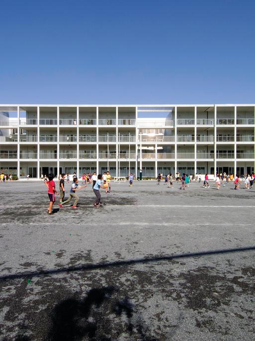 Ein fast gläsernes Gebäude, eine Schule, von dem japanischen Architekten Riken Yamamoto entworfen. Davor laufen viele Kinder.