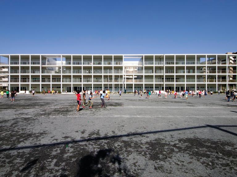 Ein fast gläsernes Gebäude, eine Schule, von dem japanischen Architekten Riken Yamamoto entworfen. Davor laufen viele Kinder.