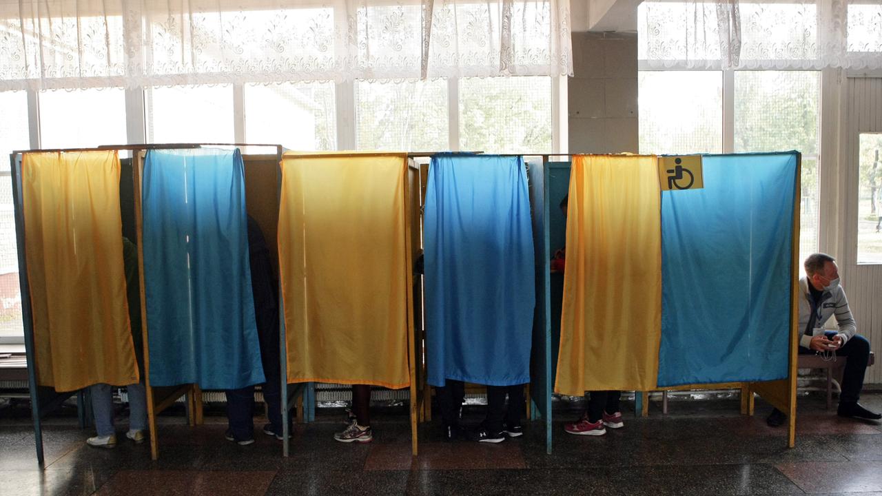 Blaue und gelbe Vorhänge an Wahlkabinen vor einem Fenster. Blaue und gelbe Vorhänge an Wahlkabinen vor einem Fenster.