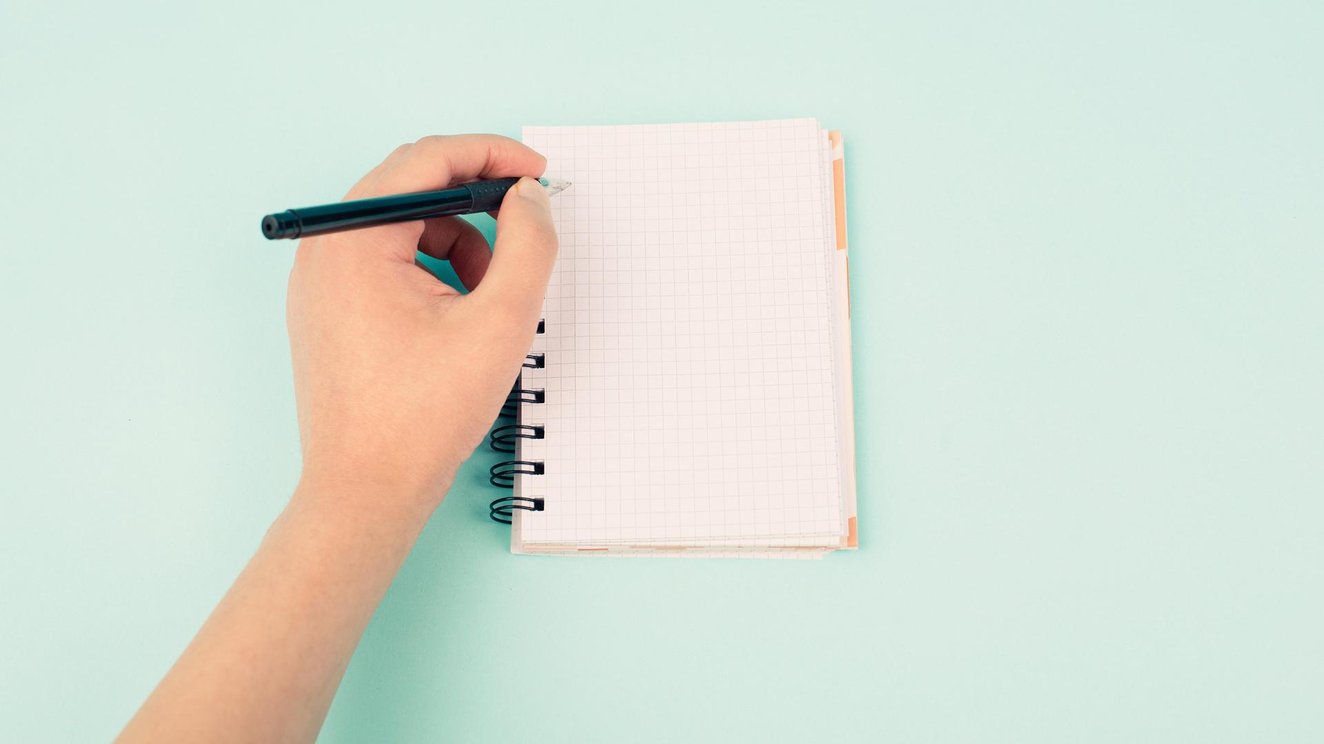 Die linke Hand hält einen Stift, mit dem in ein Notizbuch geschrieben wird.