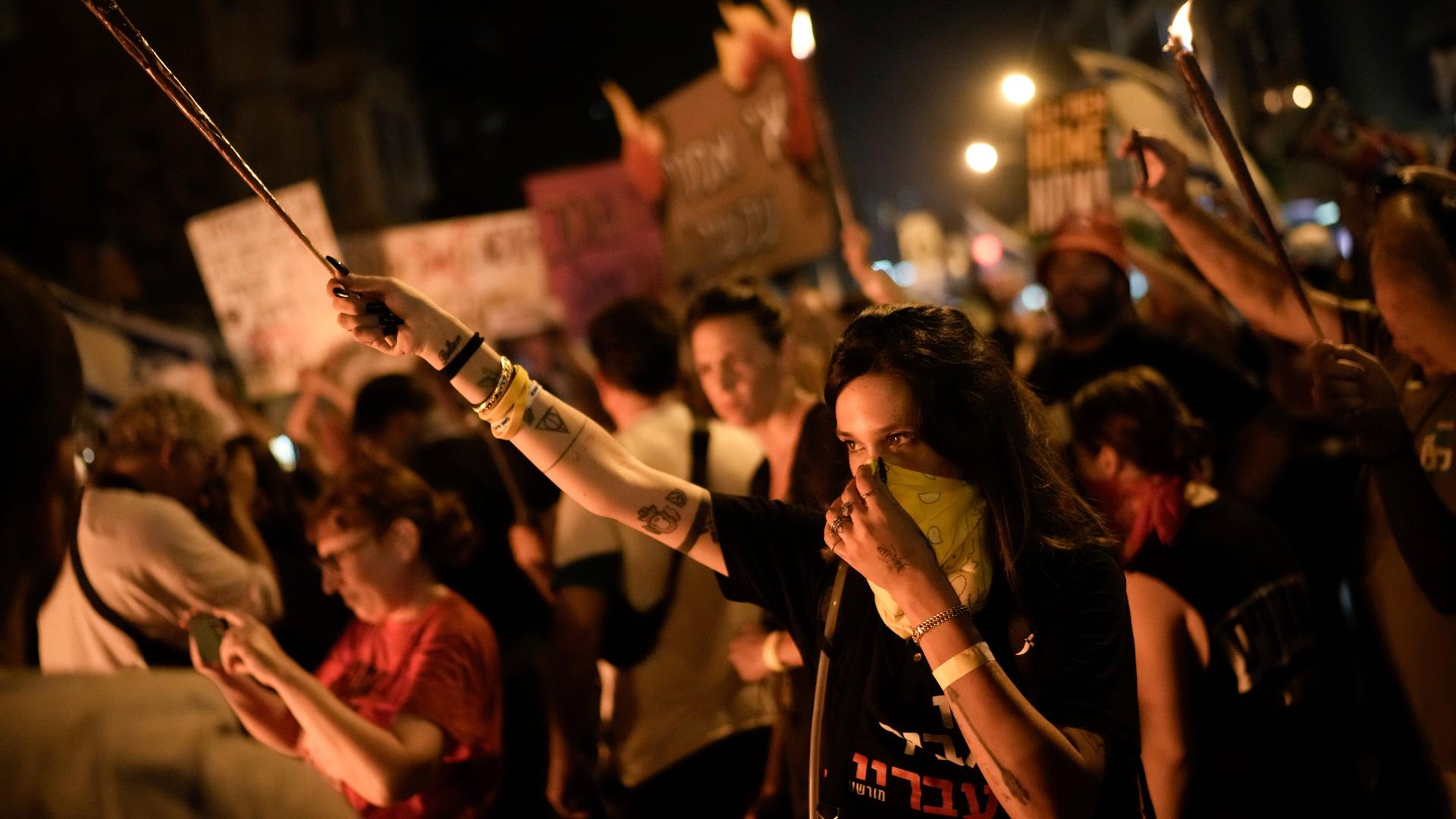 Es ist dunkel; die Demonstranten sind beleuchtet. Im Vordergrund eine junge Frau, die eine Fackel hochhält und ein Tuch über Mund und nase zieht.