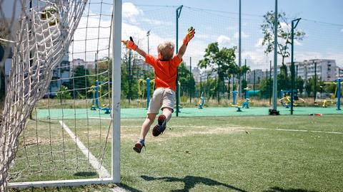 Ein Kind in Fußballkleidung beim Sprung durch die Luft vor einem Tor.