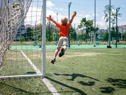 Ein Kind in Fußballkleidung beim Sprung durch die Luft vor einem Tor.