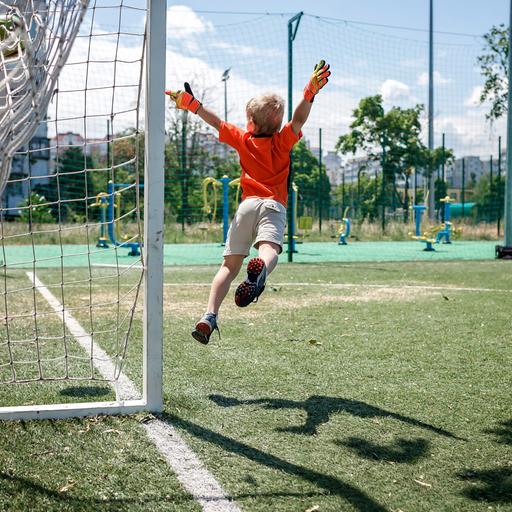 Ein Kind in Fußballkleidung beim Sprung durch die Luft vor einem Tor.