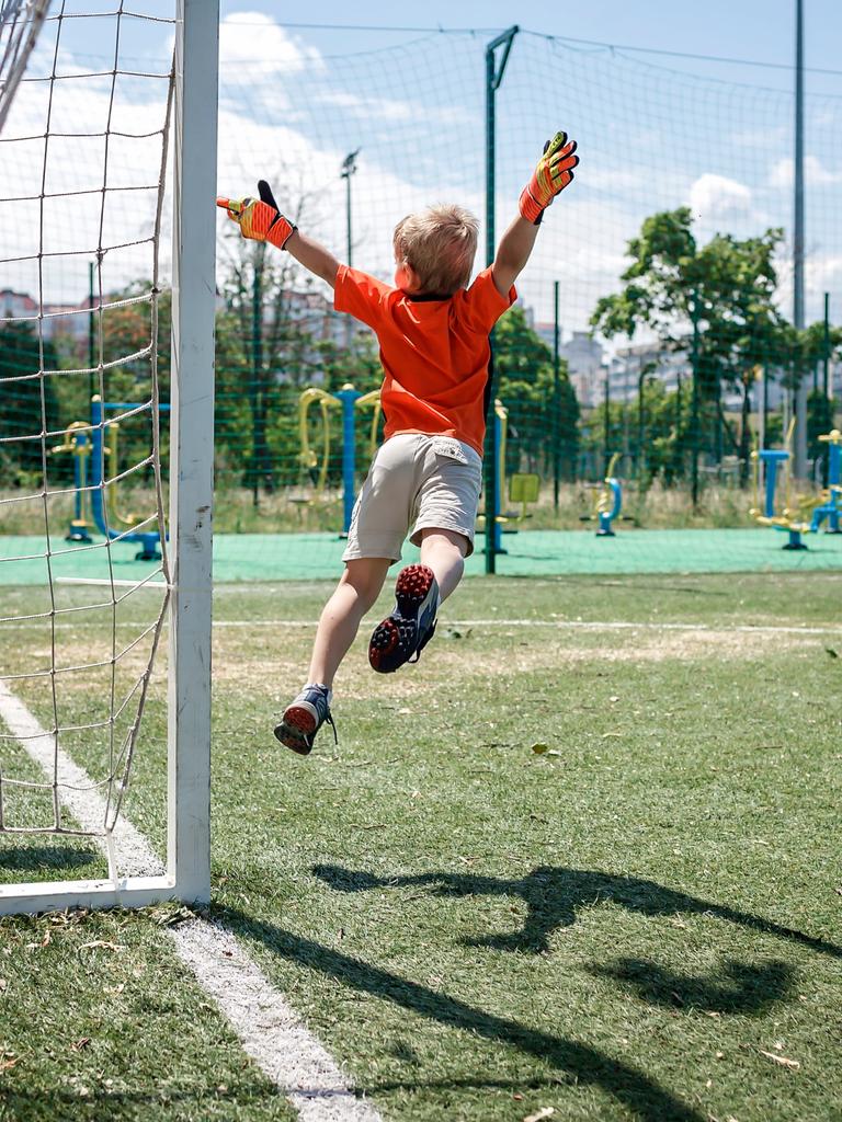 Ein Kind in Fußballkleidung beim Sprung durch die Luft vor einem Tor.