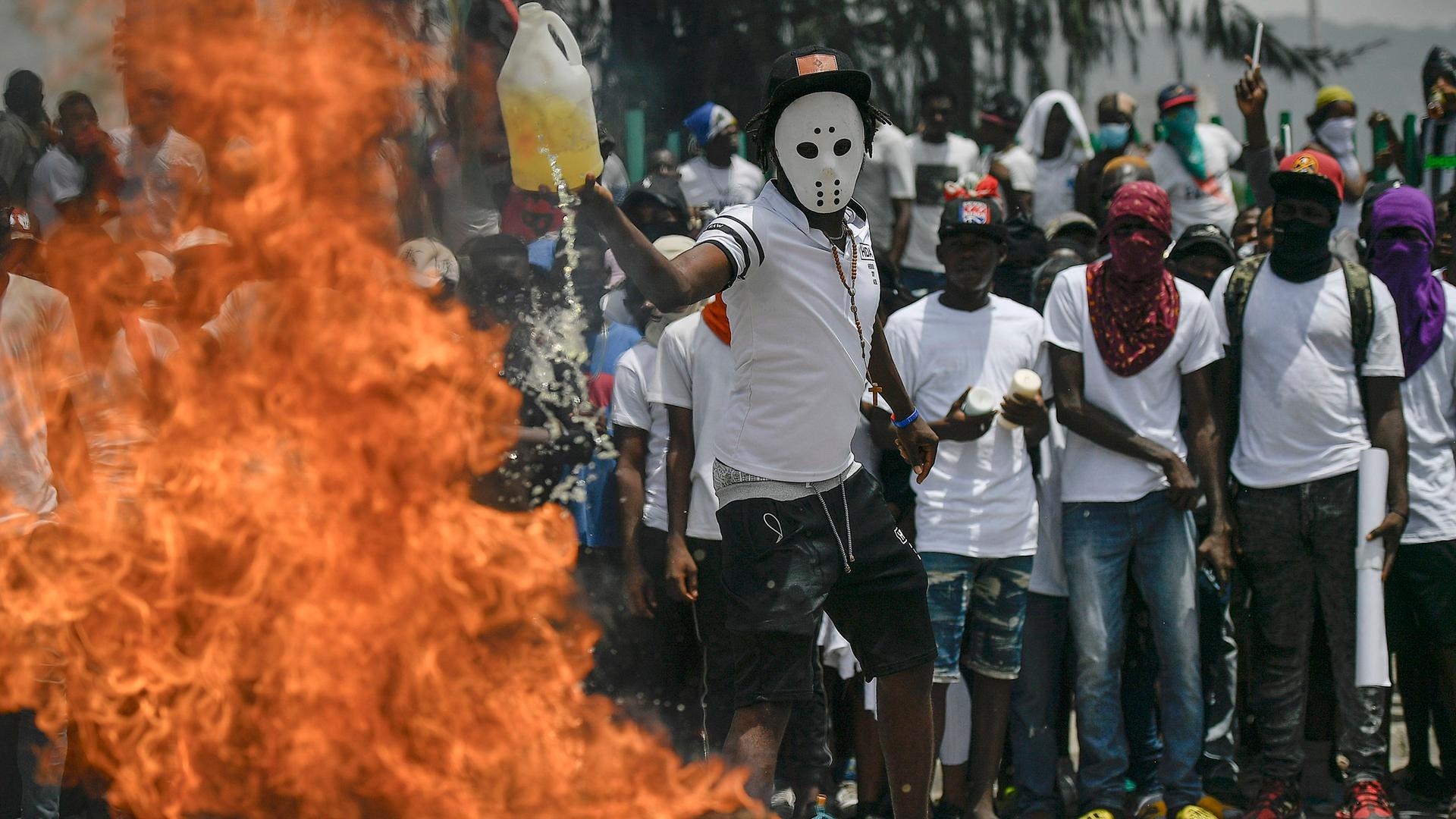 Mehrere maskierte Menschen stehen vor einer brennenden Barrikade in Haitis Hauptstadt Port-au-Prince.
