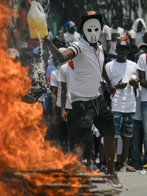 Mehrere maskierte Menschen stehen vor einer brennenden Barrikade in Haitis Hauptstadt Port-au-Prince.