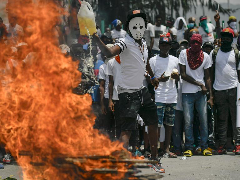 Mehrere maskierte Menschen stehen vor einer brennenden Barrikade in Haitis Hauptstadt Port-au-Prince.