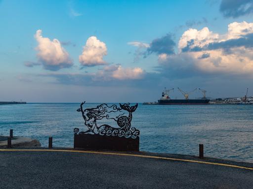 Szene an einer Uferpromenade auf Kreta. Eine Meerjungfrauinstallation ist vor dem Meer zu sehen.