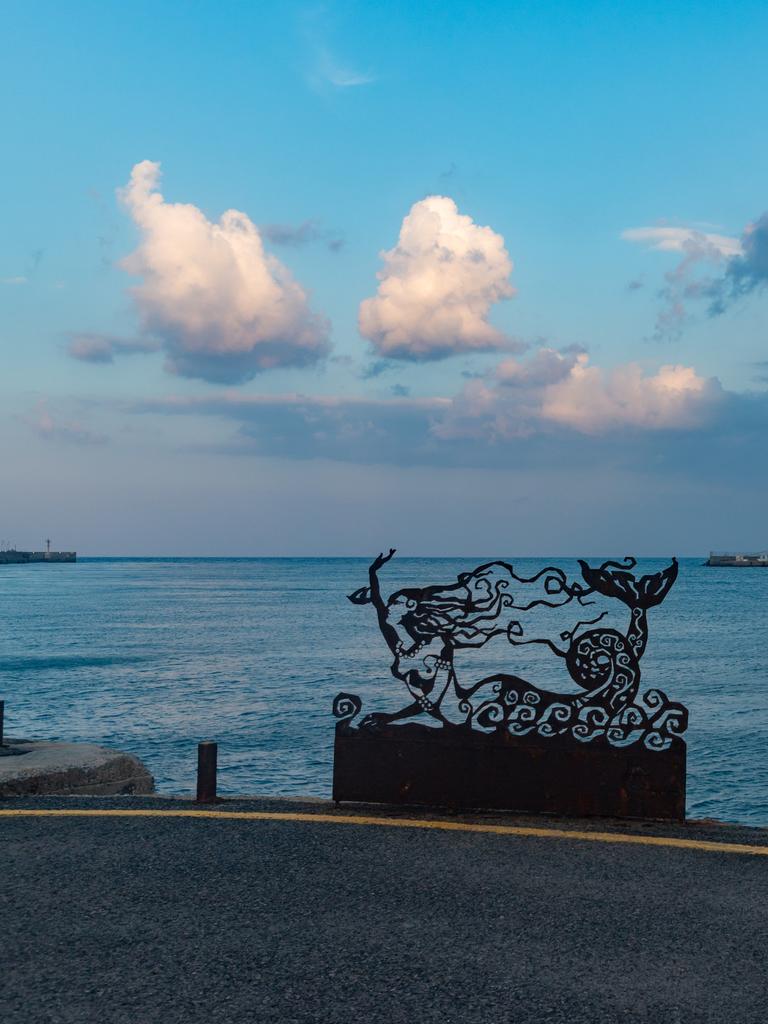 Szene an einer Uferpromenade auf Kreta. Eine Meerjungfrauinstallation ist vor dem Meer zu sehen.