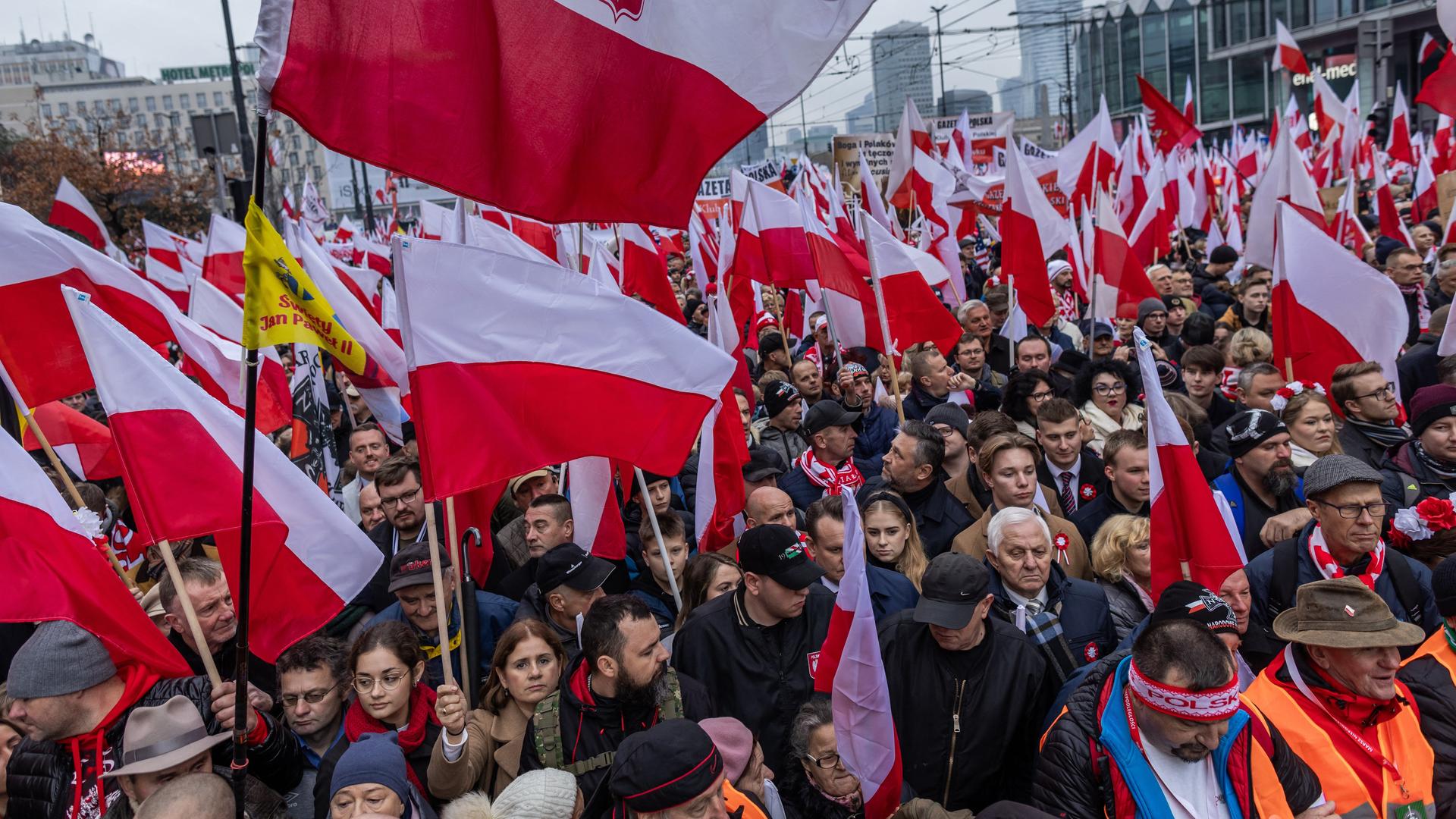 In Warschau ziehen viele Menschen durch die Straßen. Sie tragen polnische Nationalflaggen. In Warschau ziehen viele Menschen durch die Straßen. Sie tragen polnische Nationalflaggen.