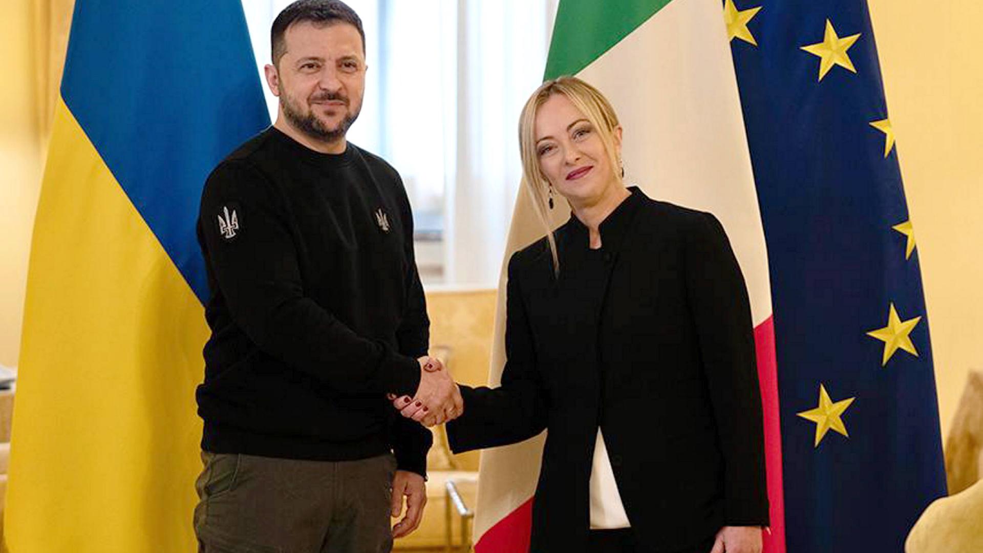 Das Foto zeigt Italiens Ministerpräsidentin Meloni und den ukrainischen Präsidenten Selenskyj. Die Politiker begrüßen sich per Handschlag, im Hintergrund sind die Nationalflaggen der beiden Staaten zu sehen. Das Foto zeigt Italiens Ministerpräsidentin Meloni und den ukrainischen Präsidenten Selenskyj. Die Politiker begrüßen sich per Handschlag, im Hintergrund sind die Nationalflaggen der beiden Staaten zu sehen.