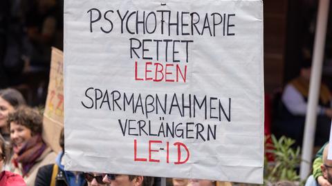 Ein Demonstrationsschild mit der Aufschrift "Psychotherapie rettet Leben. Sparmaßnahmen verlängern Leid" wird bei einer Kundgebung hochgehalten.