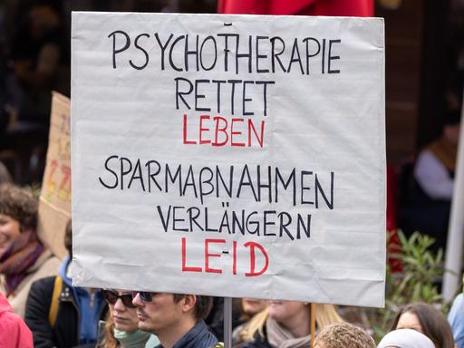 Ein Demonstrationsschild mit der Aufschrift "Psychotherapie rettet Leben. Sparmaßnahmen verlängern Leid" wird bei einer Kundgebung hochgehalten.
