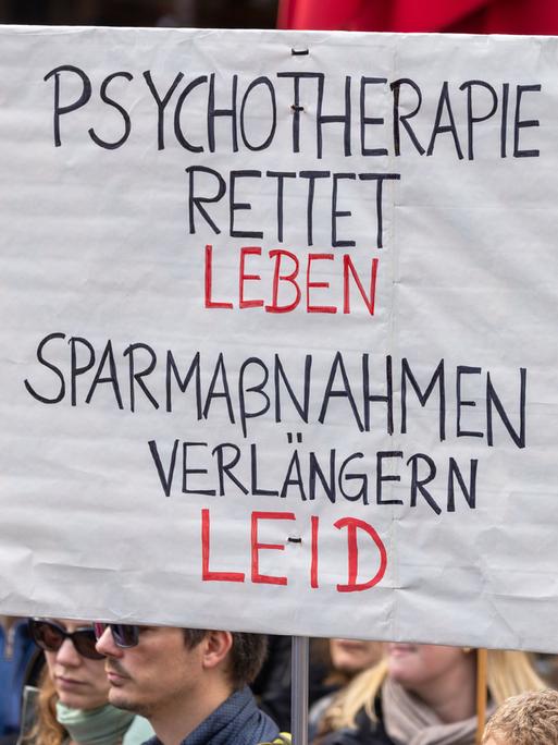 Ein Demonstrationsschild mit der Aufschrift "Psychotherapie rettet Leben. Sparmaßnahmen verlängern Leid" wird bei einer Kundgebung hochgehalten.