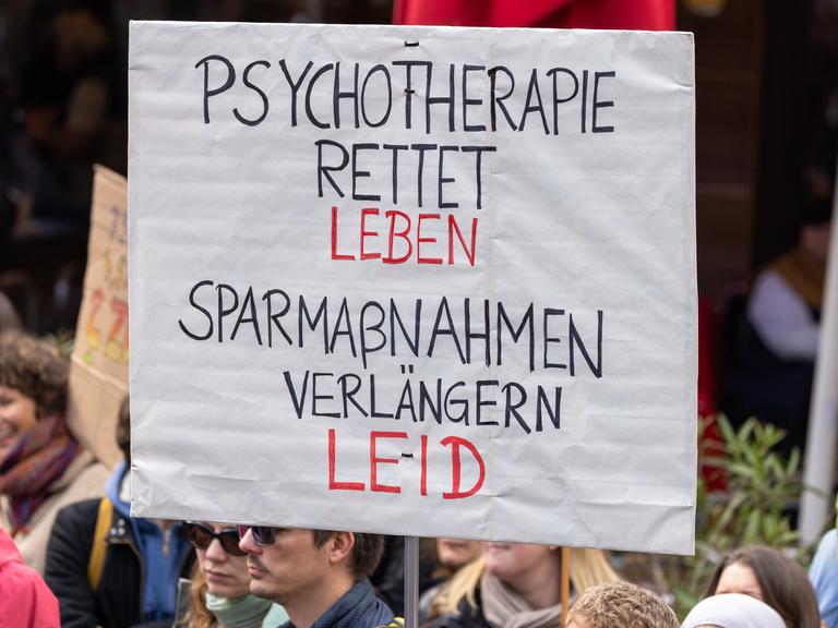 Ein Demonstrationsschild mit der Aufschrift "Psychotherapie rettet Leben. Sparmaßnahmen verlängern Leid" wird bei einer Kundgebung hochgehalten.