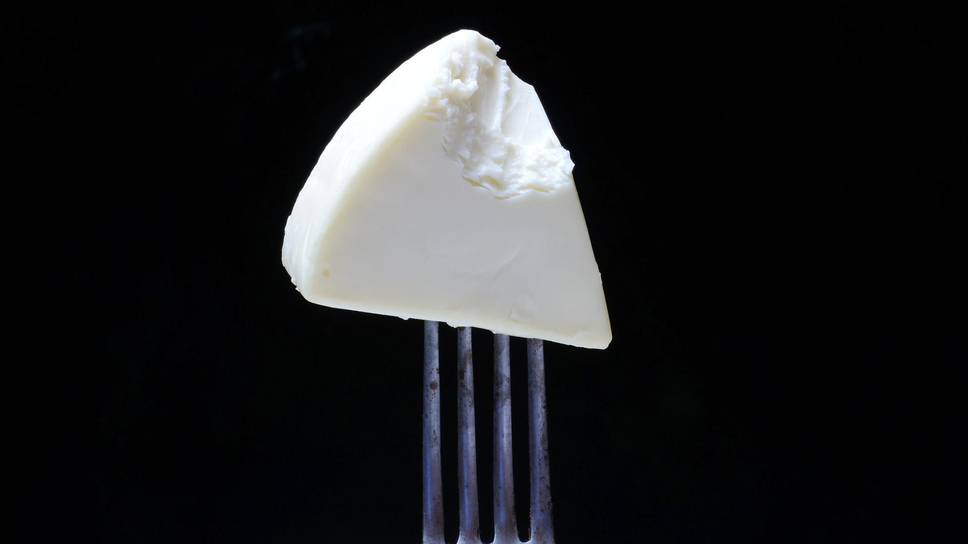 Ein angebissenes Stück Käse auf einer Gabel.