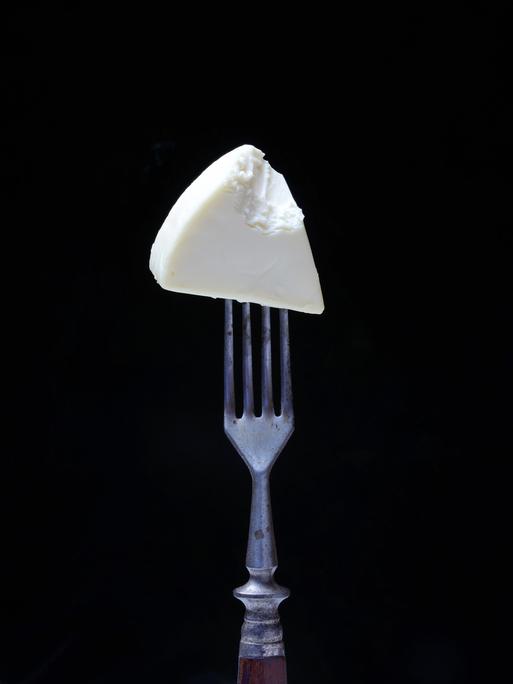 Ein angebissenes Stück Käse auf einer Gabel.