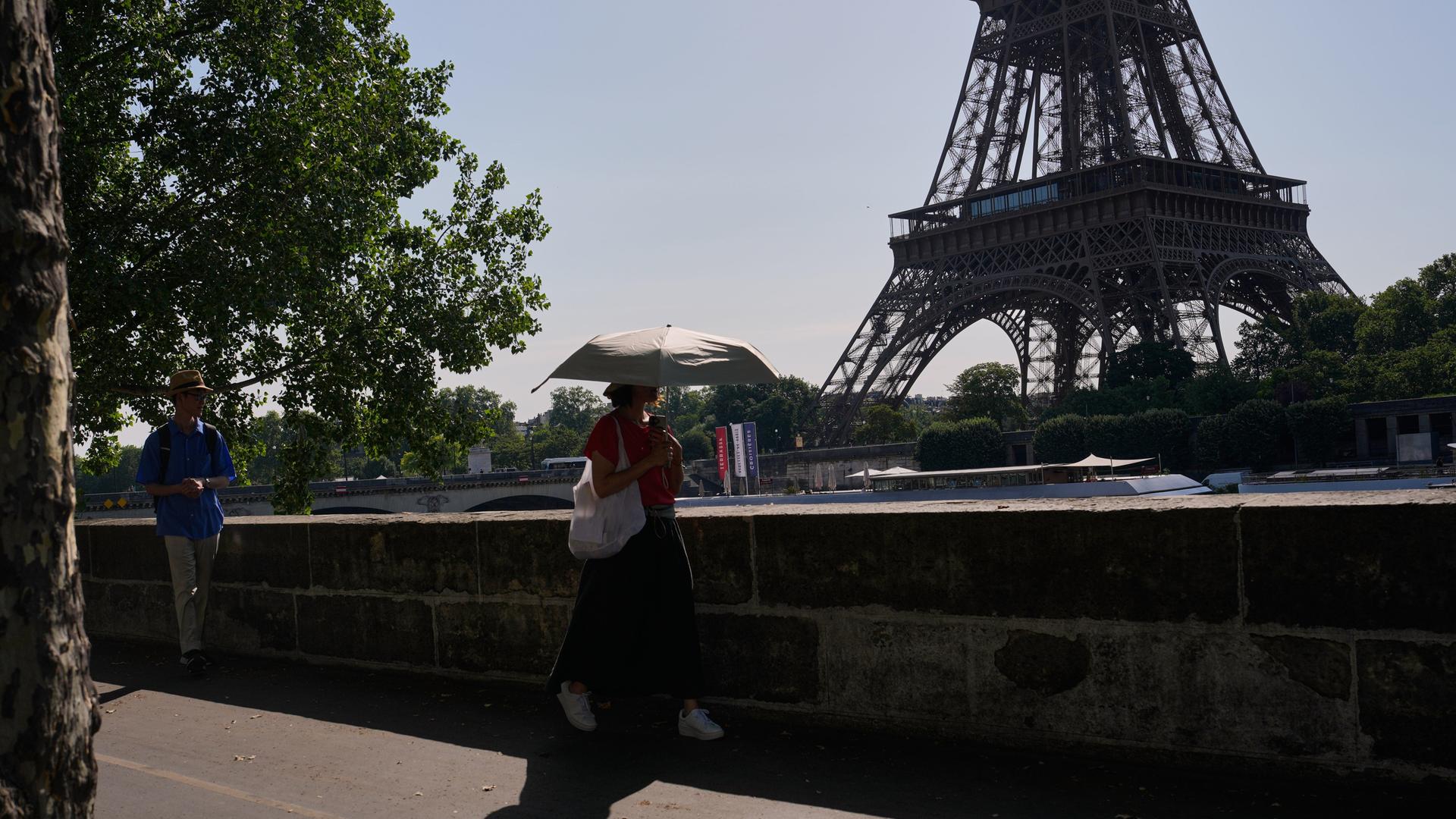 Eine Frau schützt sich mit einem Sonnenschirm vor der Sonne, während sie in der Nähe des Eiffelturms in Paris spazieren geht. 