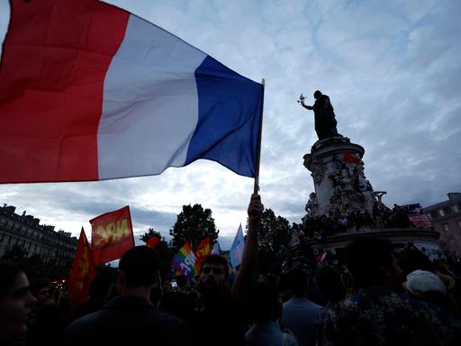 Menschen versammeln sich auf der Place de la République nach den Parlamentswahlen in Frankreich. Eine große französiche Nationalflagge weht neben der Mariannen-Statue. 