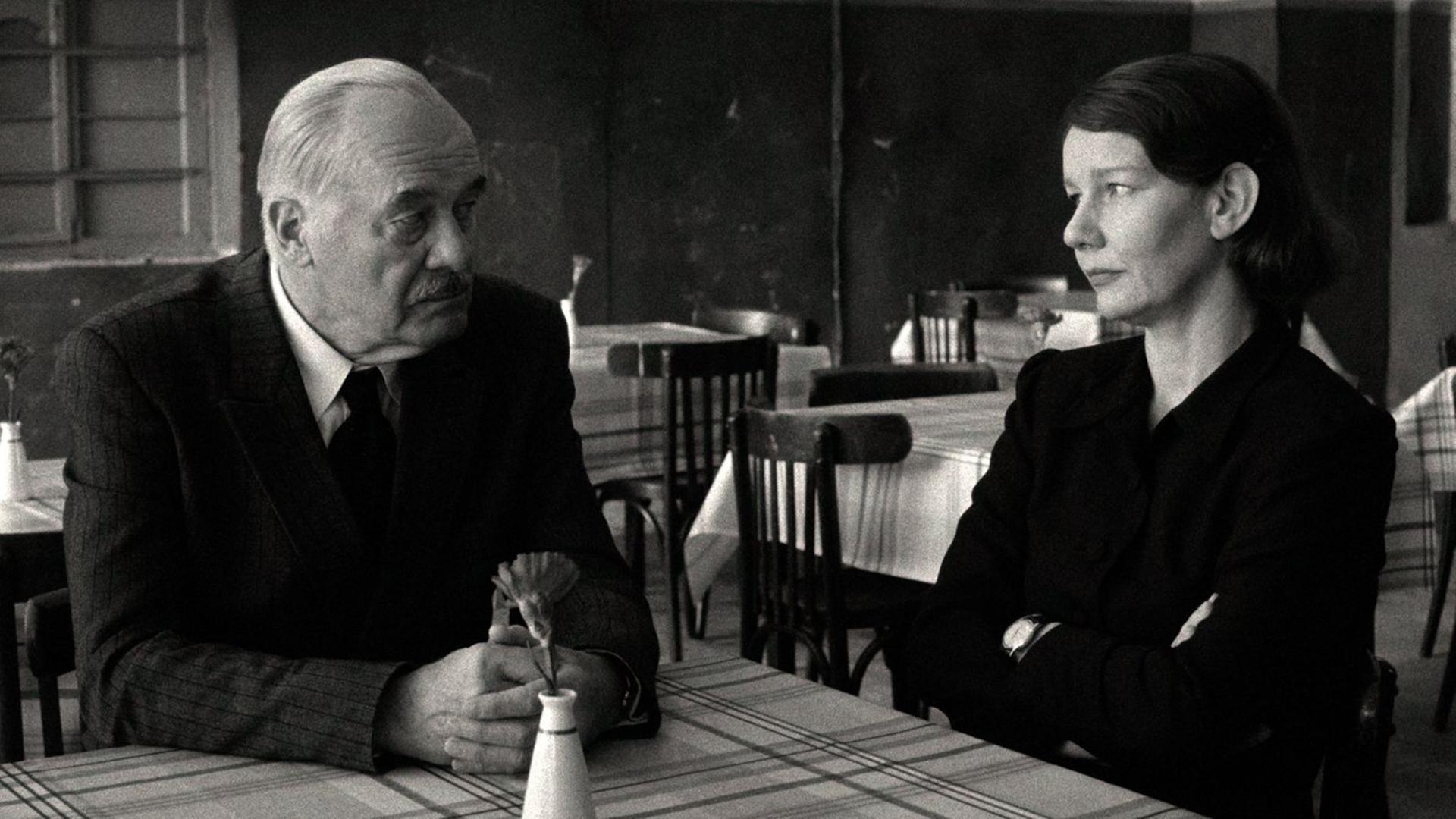 Szene aus einem Schwarz-Weiß-Film: Ein Mann und eine Frau sitzen an einem Tisch und schauen sich an. Szene aus einem Schwarz-Weiß-Film: Ein Mann und eine Frau sitzen an einem Tisch und schauen sich an.