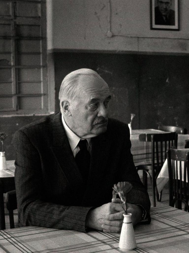 Szene aus einem Schwarz-Weiß-Film: Ein Mann und eine Frau sitzen an einem Tisch und schauen sich an.