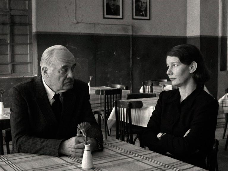 Szene aus einem Schwarz-Weiß-Film: Ein Mann und eine Frau sitzen an einem Tisch und schauen sich an. Szene aus einem Schwarz-Weiß-Film: Ein Mann und eine Frau sitzen an einem Tisch und schauen sich an.