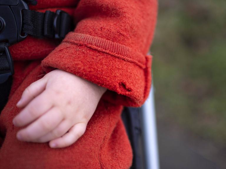 Eine Kinderhand schaut aus einem roten Mantelärmel. Der Ärmel hat ein großes Loch.