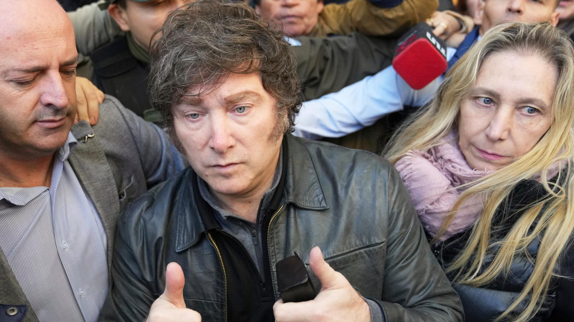 Argentiniens Präsident Milei hält beide Daumen nach oben. Er ist umringt von mehreren Personen. 