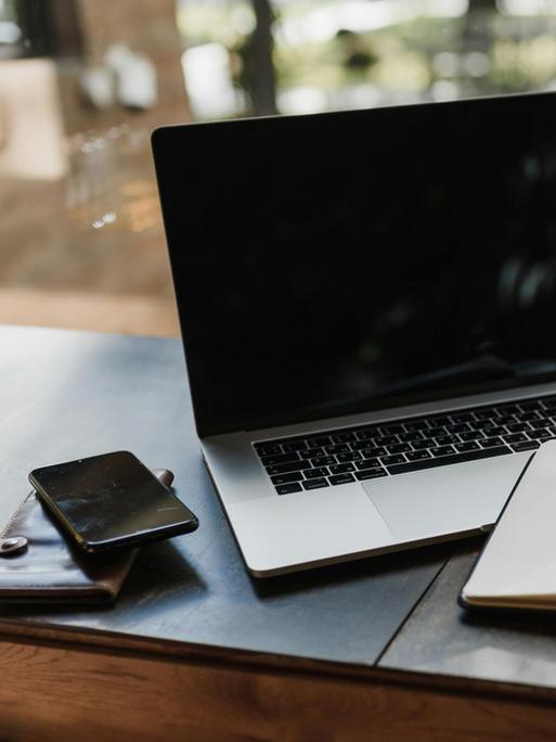 Blick auf einen Arbeitsplatz mit Laptop, Handy, Notizbuch, Stift, Brille und einer Tasse Kaffee.