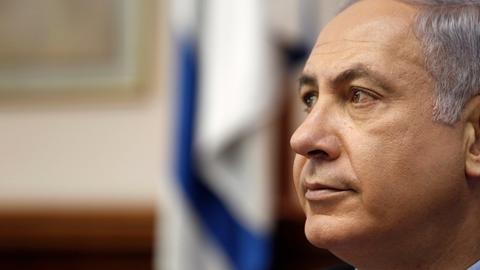 Portrait von Benjamin Netanjahu, im Hintergrund in der Unschärfe die israelische Flagge